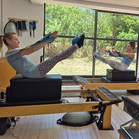 Client stretching on a Pilates reformer in a warm indoor studio