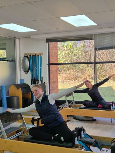 Two women kneeling on reformers in a side stretch